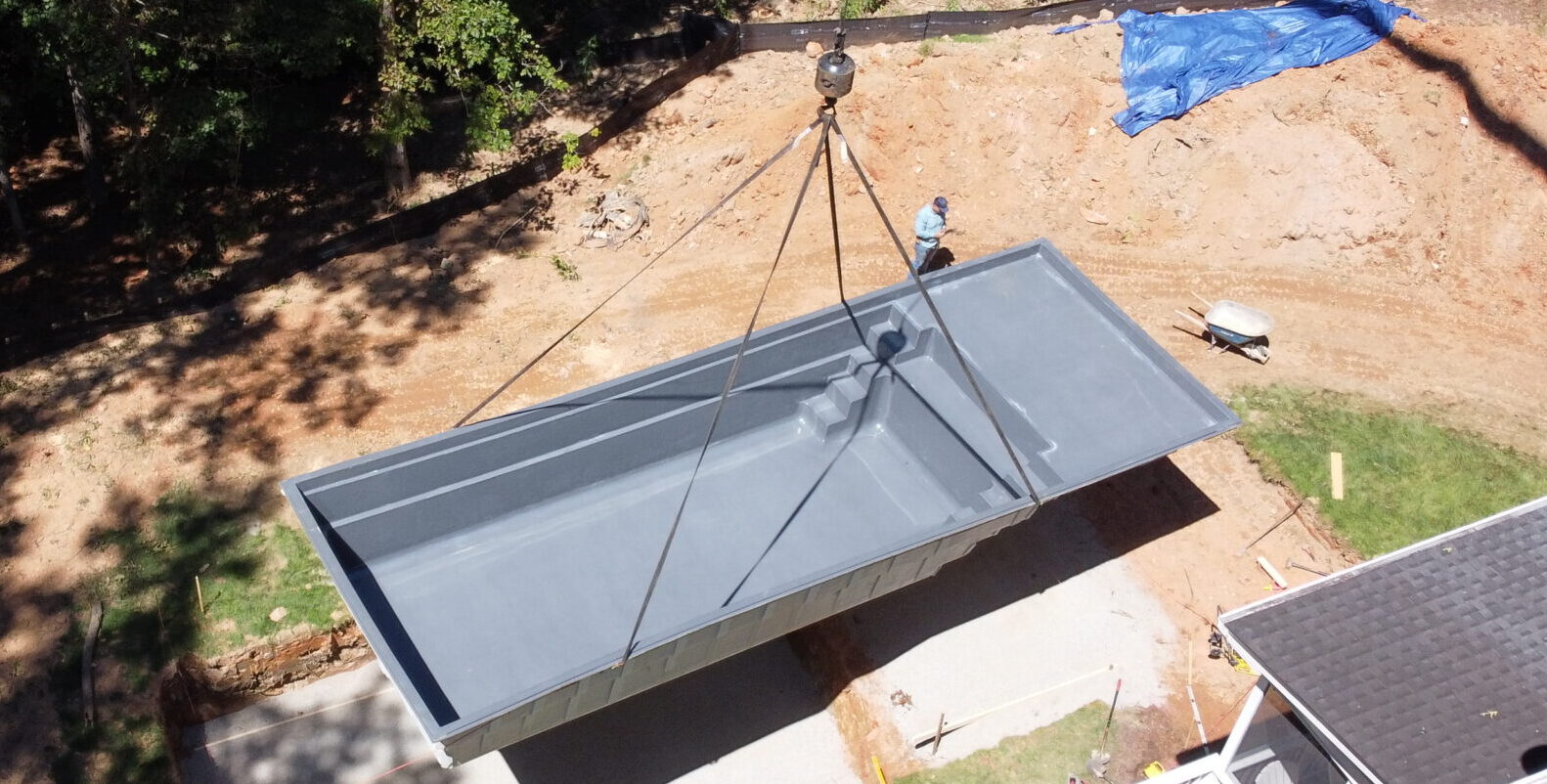 Backyard project in progress featuring a fiberglass pool shell being installed into the excavated hole.