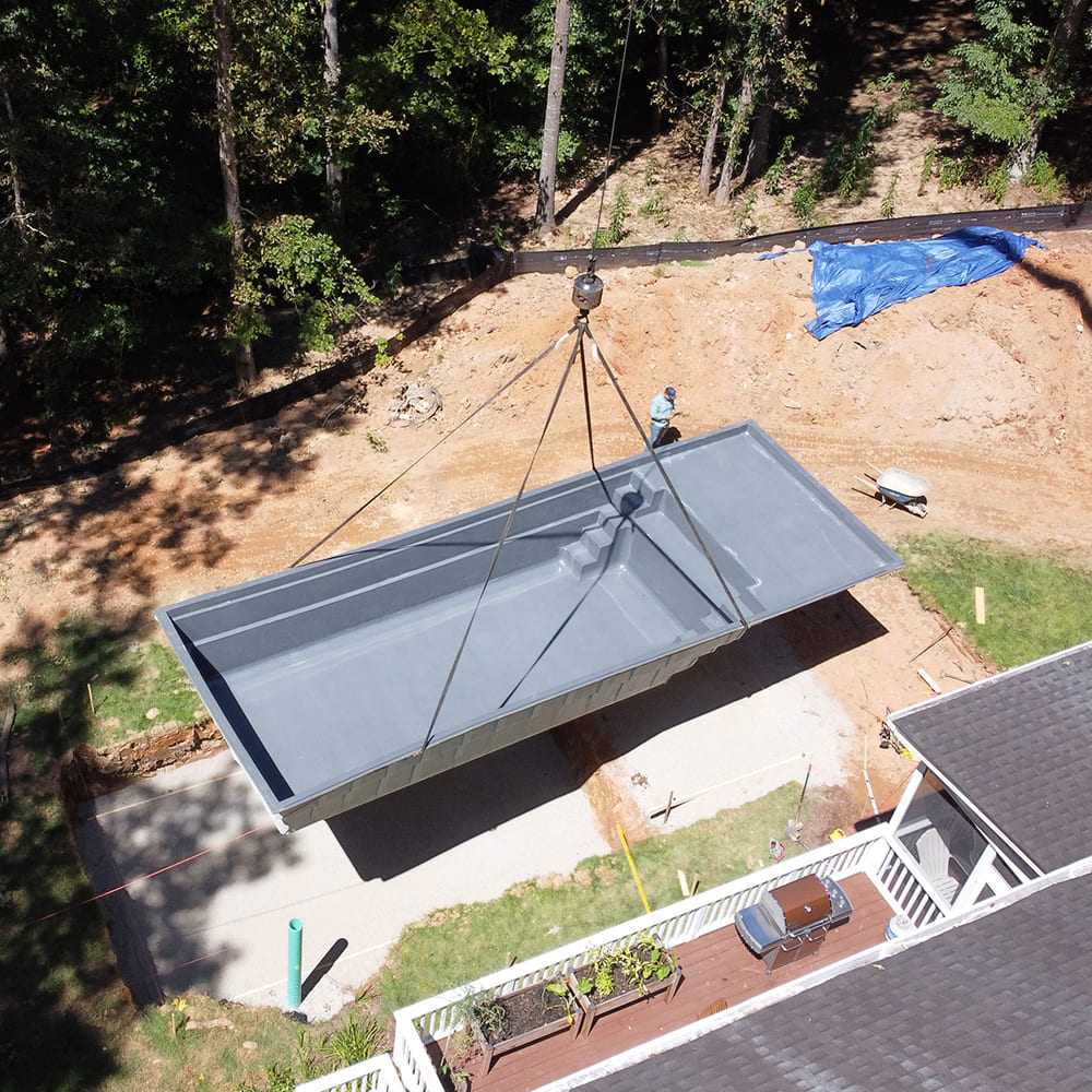 Backyard project in progress featuring a fiberglass pool shell being installed into the excavated hole.